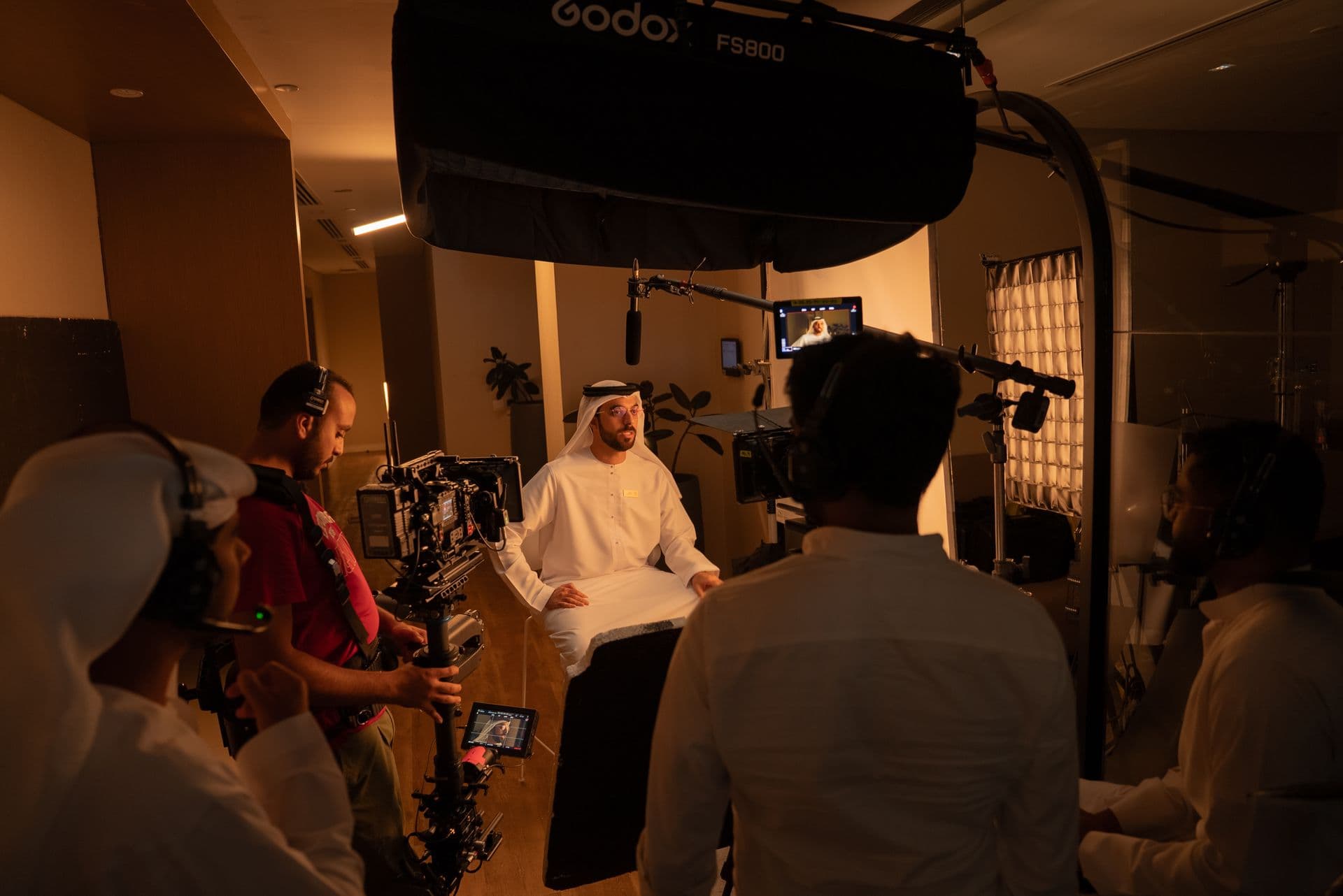 A crew behind the camera in a warm-lit room