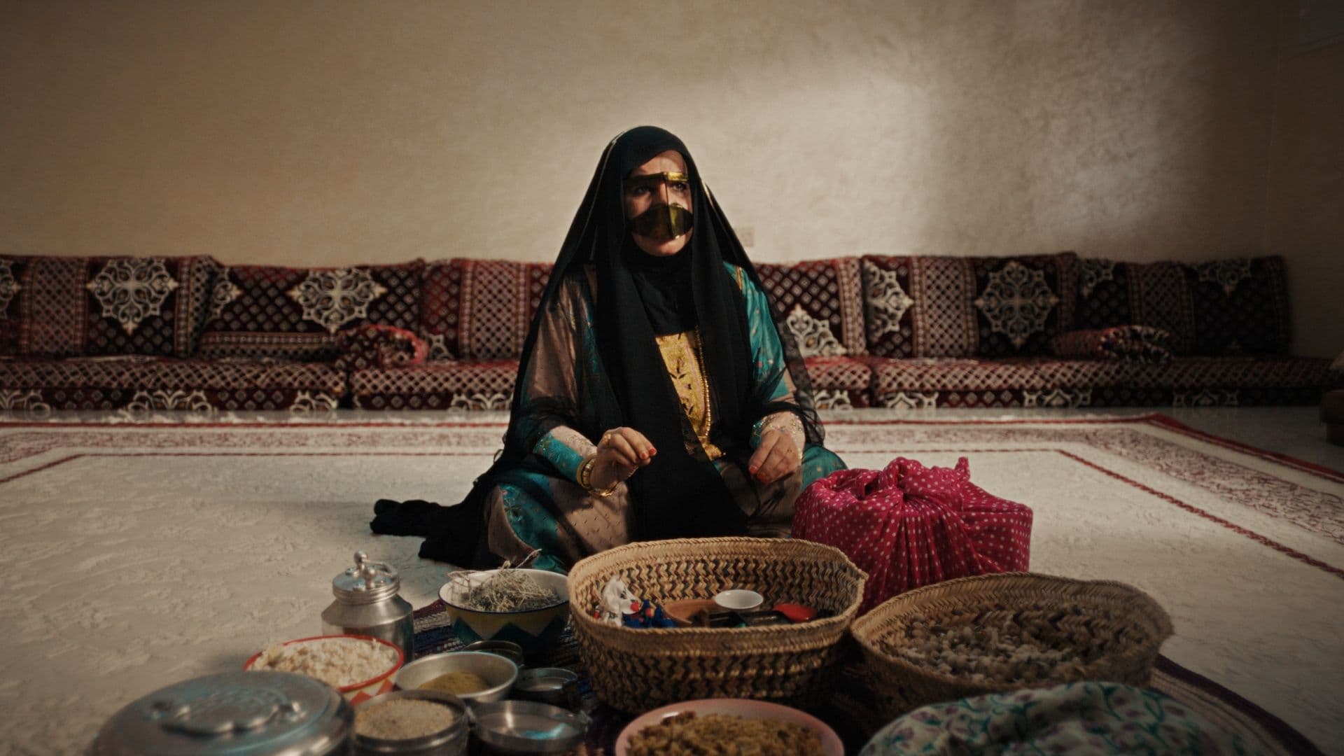 A woman in a gold burqa seated among baskets in a majlis